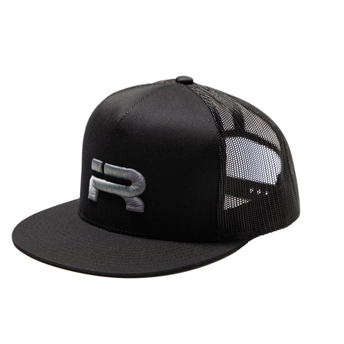 A black trucker-style snapback cap with a structured black front panel, black flat brim, and black mesh back panels. A stylized silver 'R' logo is embroidered on the front panel.