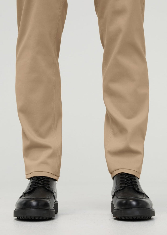 Khaki tapered trousers with visible center seams, cuffed at ankles, worn with black lace-up shoes.