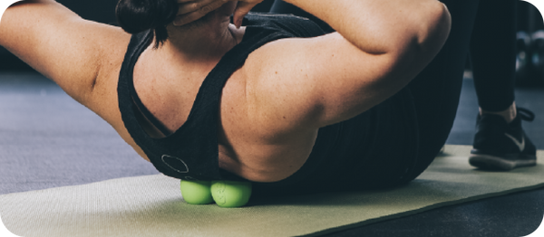 Person using green massage balls under upper back on a yoga mat for muscle release and recovery with the RAD Roller Original | RAD.