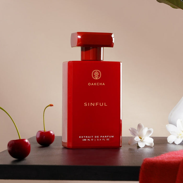 Front view of Sinful perfume bottle showcasing glossy red rectangular bottle and cap with cherries and white flowers on beige background